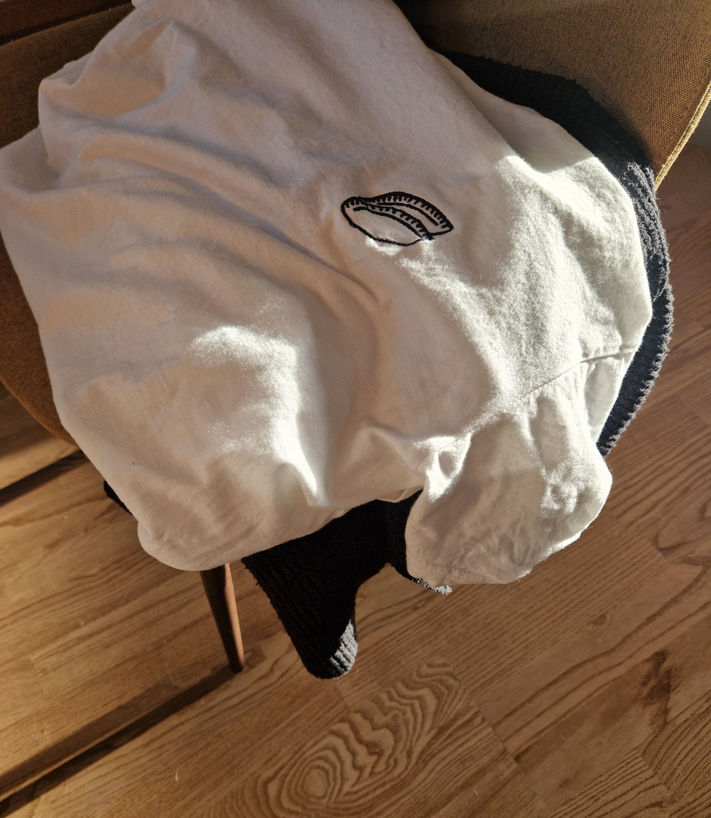 White t-shirt with an embroidery of an empanada on a wooden chair