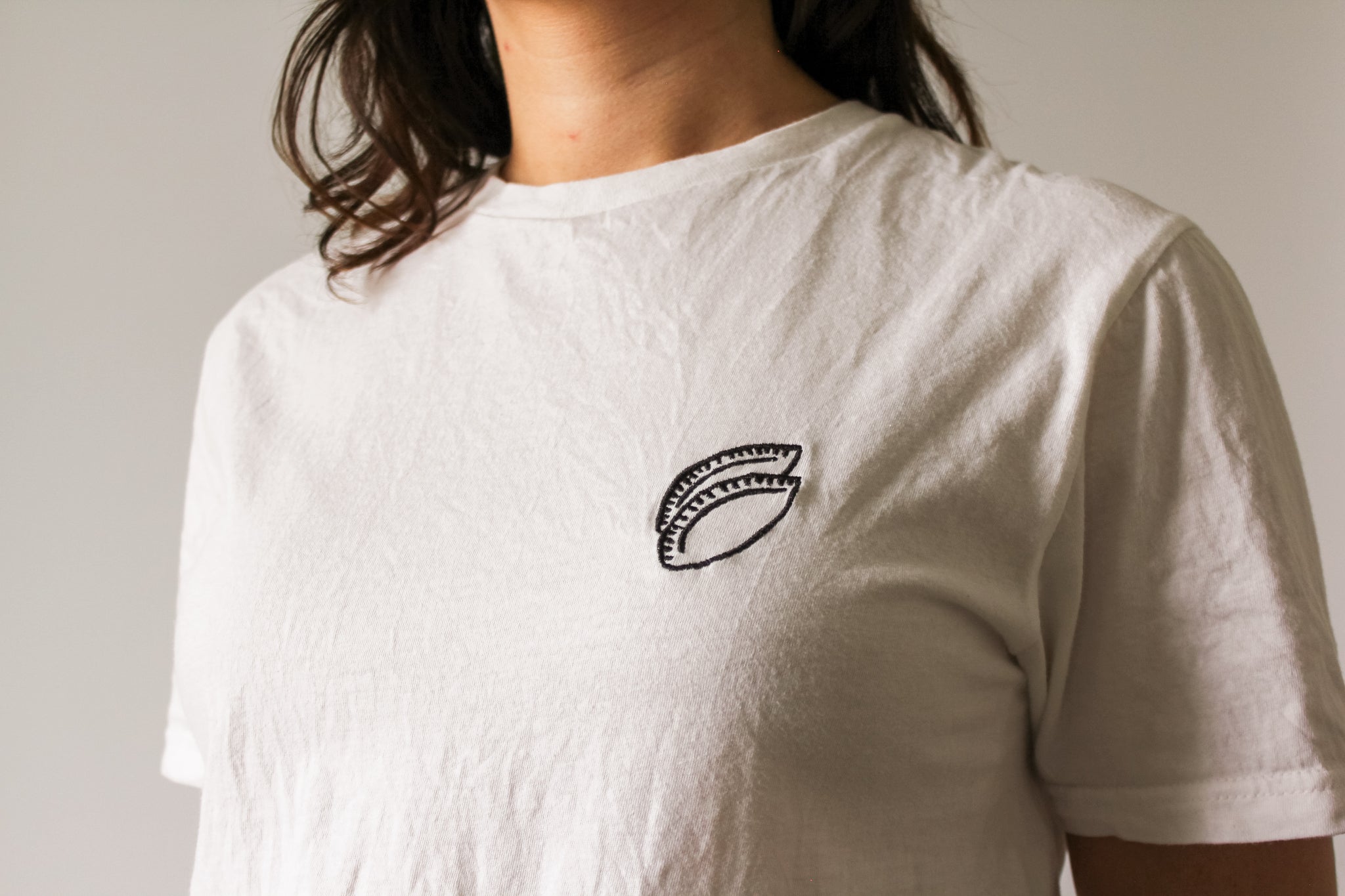 White t-shirt with a black empanada embroidery worn by a person on a plain background