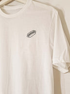 White t-shirt with a small black hot dog embroidery on a beige background
