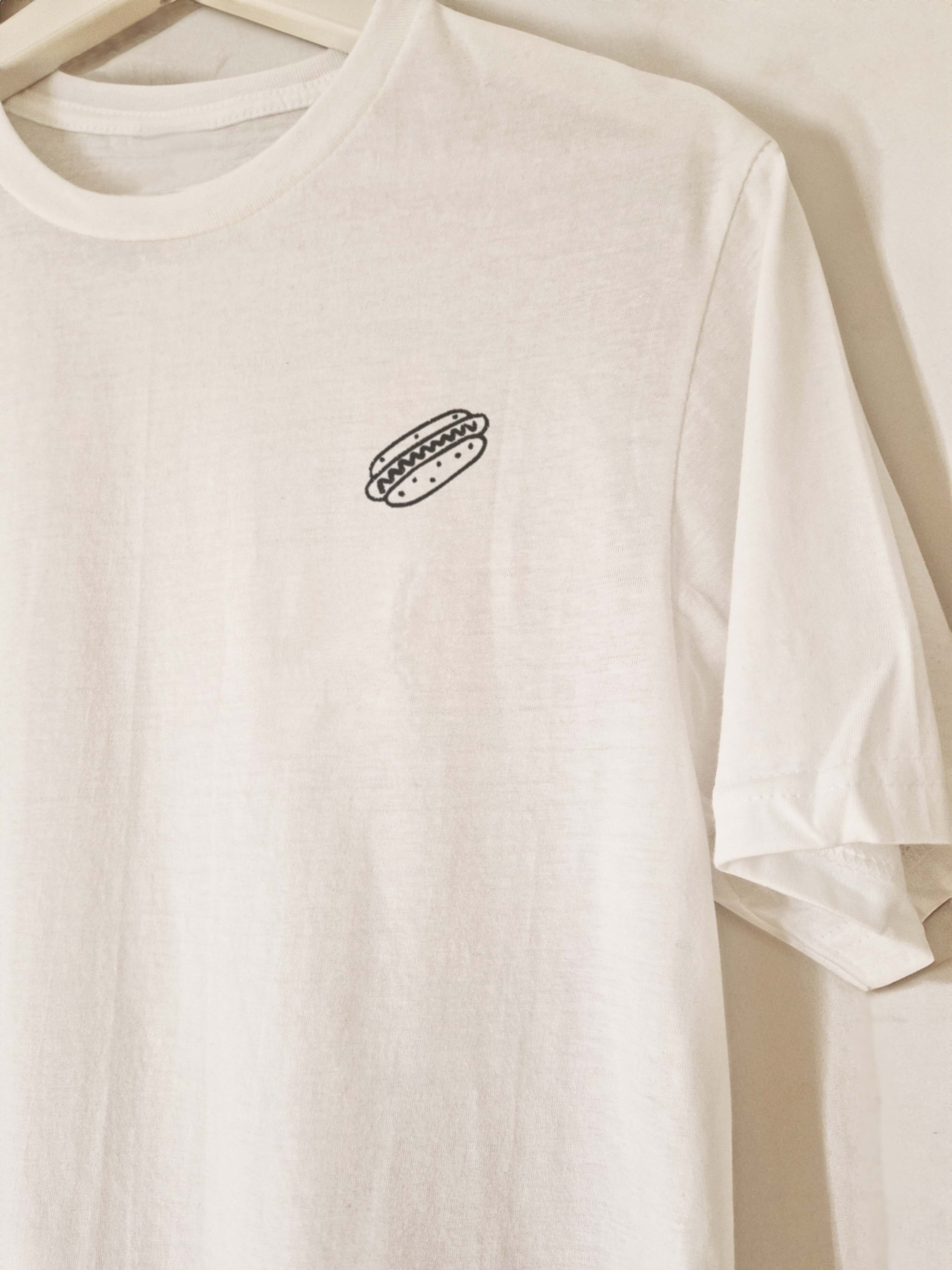 White t-shirt with a small black hot dog embroidery on a beige background