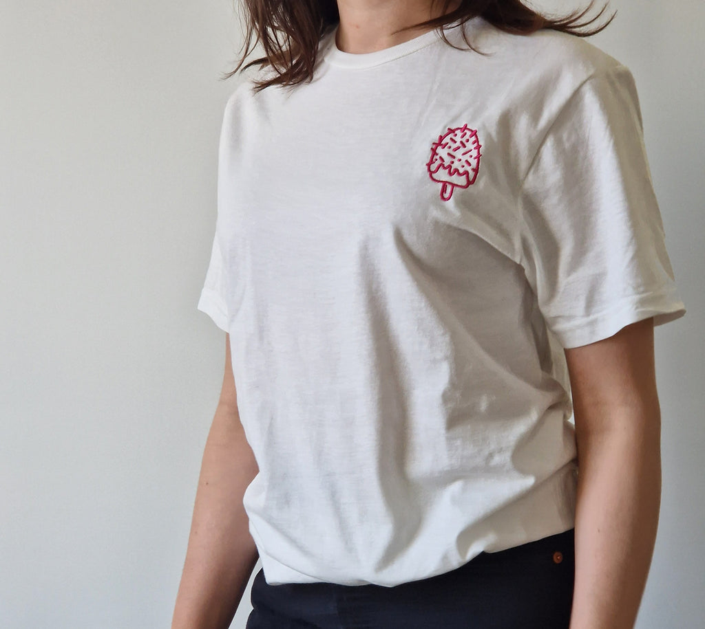 Person wearing a white t-shirt with a pink ice cream cone embroidery on a plain background