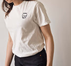 Person wearing a white t-shirt with a small pickles embroidery on a plain background