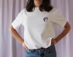 Person wearing a white t-shirt with a small logo on a plain background